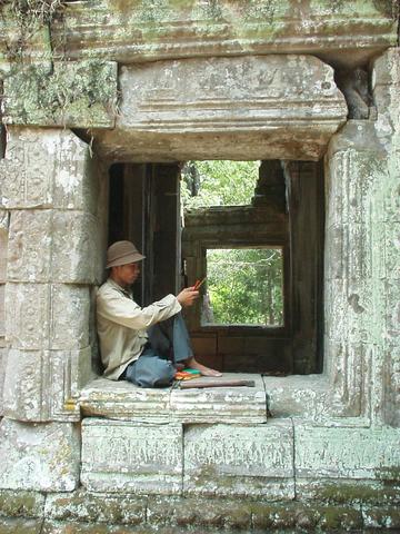 Cambodian man lounging in a window at Ta Prohm, Angkor.