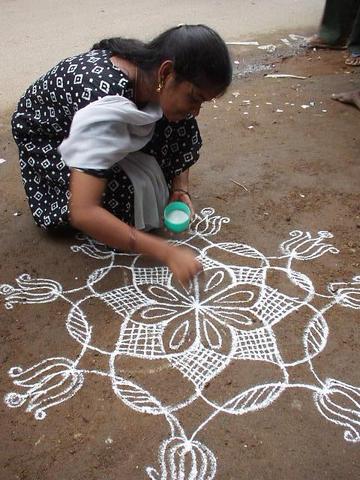 Woman drawing a Kolam outside of her business, Madurai.